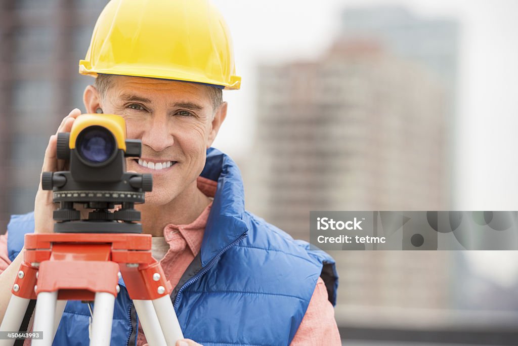 Happy Mature Construction Worker With Theodolite Portrait of happy mature construction worker with theodolite standing at construction site 40-44 Years Stock Photo