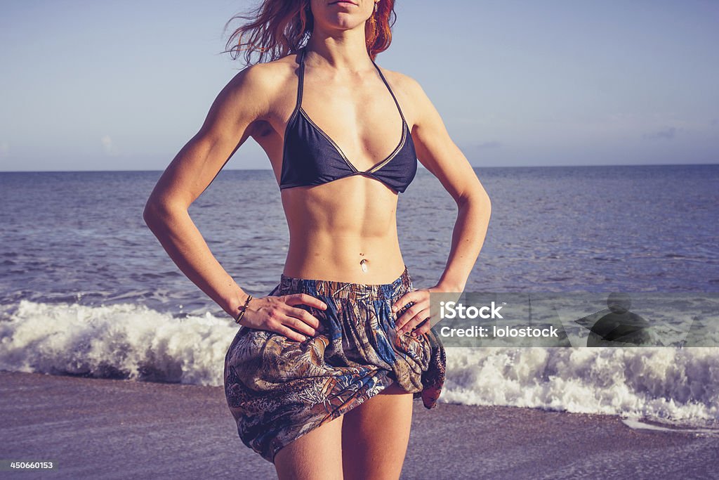 Young woman with toned abs standing on the beach Young woman with toned abs is standing on the beach with her hands on her hips Abdominal Muscle Stock Photo