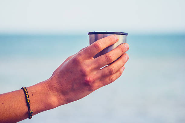 istock Woman's hand holding a thermos cup by the sea 450667669