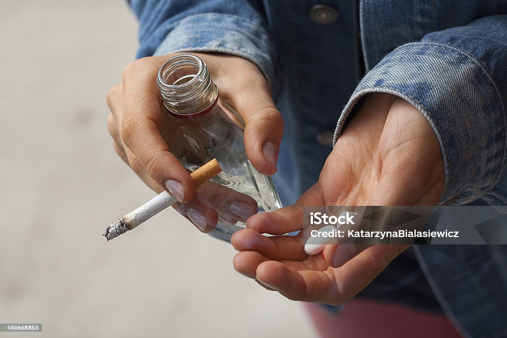 Girl holding vodka,pills and cigarettes Young woman smoking cigarettes, drinking vodka and taking pills Alcohol - Drink Stock Photo