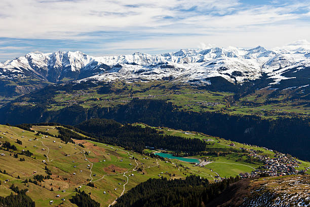 View from the mountainside down to Brigels with its lake and across the rhine valley to Obersaxen and the freshly snow-covered mountains in the background.