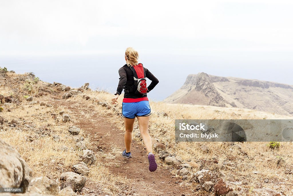 Young woman trail running in mountains Young woman running on trail in mountains on summer day. Female runner exercising outdoors in nature on La Gomera, Canary Islands. Gomera - Canary Islands Stock Photo