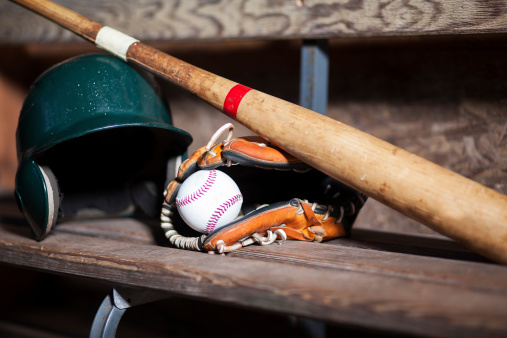 Baseball bat, Baseball, Baseball Helmet and Catchers Glove on a bench.