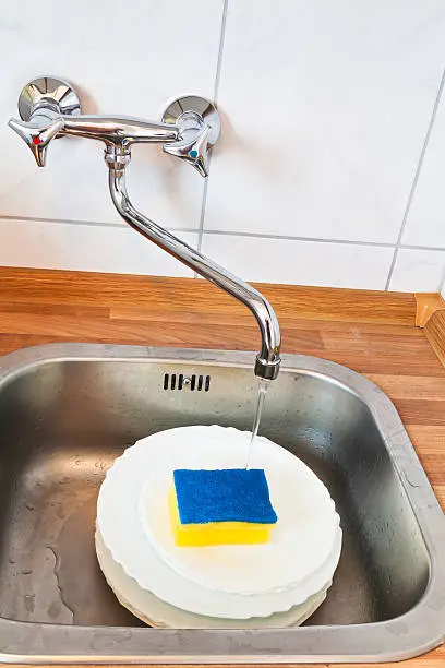 washing-up by cleaning sponge in metal washbasin in kitchen