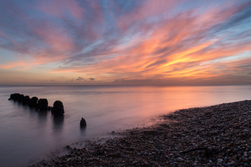 A DSLR photo of a red sky on Brighton beach at dawn. Shot with a long exposure, the sea has a misty effect where the groin protrudes through the sea