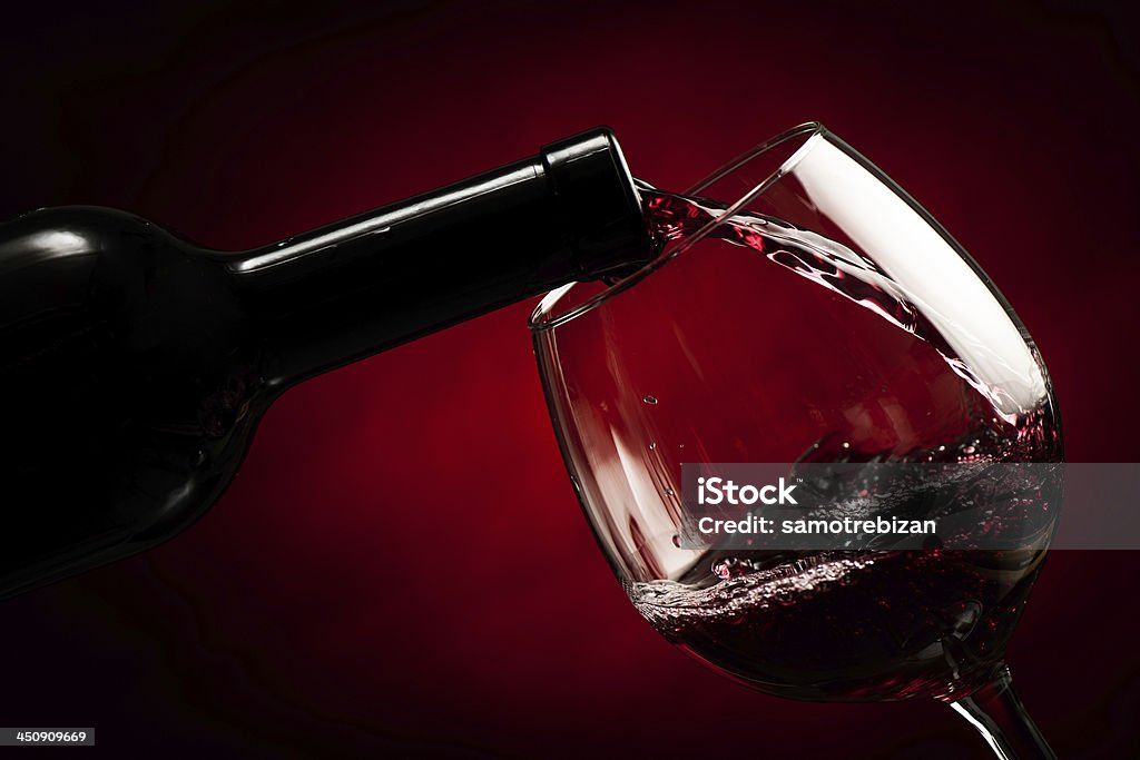 A bottle of red wine pouring into a glass Black bottle of red wine filling the glass on red background. Splash of delicious flavor.  Abstract Stock Photo