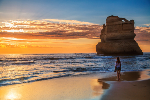 Beautiful woman looking out at sea at the Twelve Apostles, Port Campbell National Park at sunset - Victoria, Australia