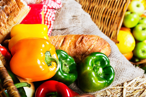 Healthy eating can be delicious! Shiny sweet peppers, fresh bread, cheese and fruit spill from wicker baskets at a farmers market.