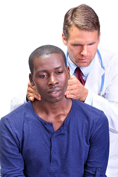 Young black man receives medical examination by white male doctor who feels the neck checking for enlarged lymph nodes