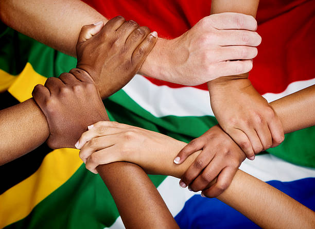 Rainbow Nation hands clasped in unity against South African flag Six mixed hands are clasped in unity against a background of the South African flag, illustrating the patriotic ideals of the Rainbow Nation.. south africa flag stock pictures, royalty-free photos & images