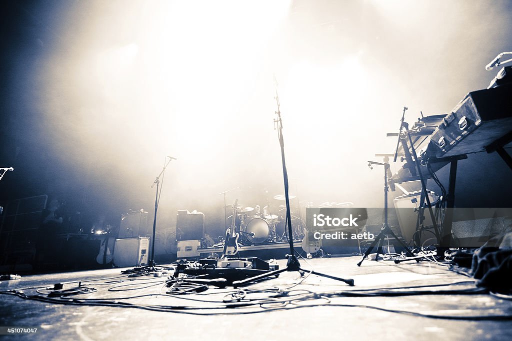 Empty stage littered with musical accessories Empty illuminated stage with drumkit, guitar and microphones Stage - Performance Space Stock Photo