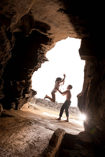 Young attractive caucasian couple jumping together in rock archway stock photo