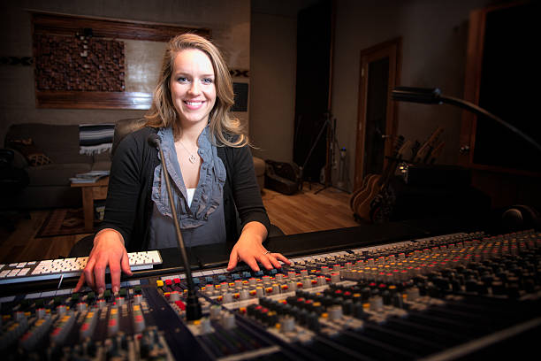 Young Blond Caucasian Woman in her 20s  Recording Console Pretty Blond American woman operating a modern digital live sound or recording console wearing professional head phones and looking forward with a big open mouth smile on her face.  Her hands are at different places on the board and other rack mounted recording gear is in the background. sound technician stock pictures, royalty-free photos & images