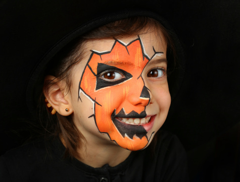 Pretty girl with face painting of a pumpkin isolated on black background
