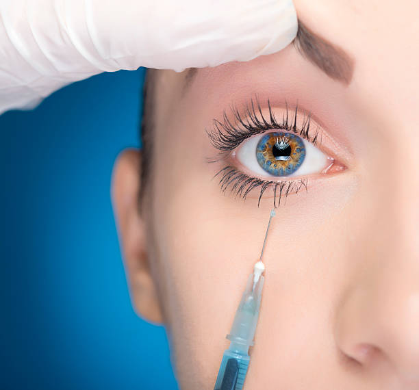 plastic surgery eyelift close-up of blue eye and doctor making injection, blue background. hazel blue eyes stock pictures, royalty-free photos & images