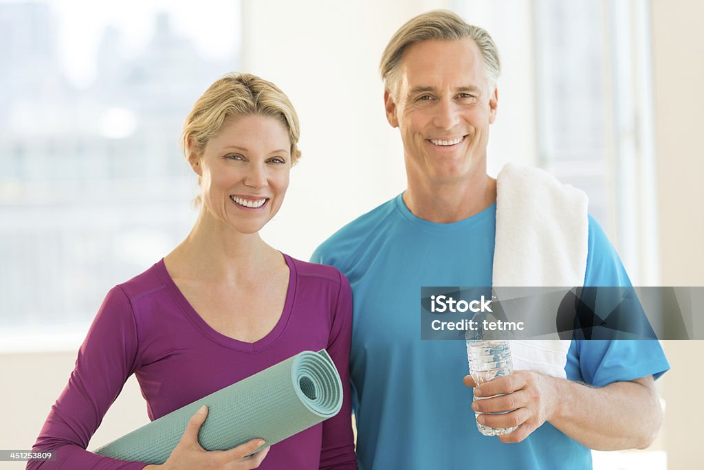 Two adults holding exercise related items Portrait of happy mature couple with exercise mat; water bottle and towel in health club Exercising Stock Photo