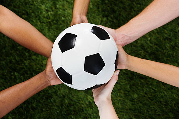 istock Many hands supporting soccer ball against grassy background. 451258667
