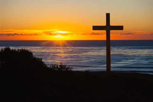 Rugged wooden cross against sunset sky at the coastline