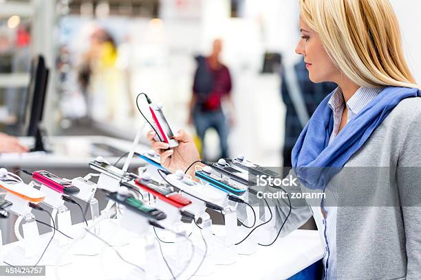 Blonden Frau Auf Der Suche Auf Smartphones Im Store Stockfoto und mehr Bilder von Elektrogeschäft
