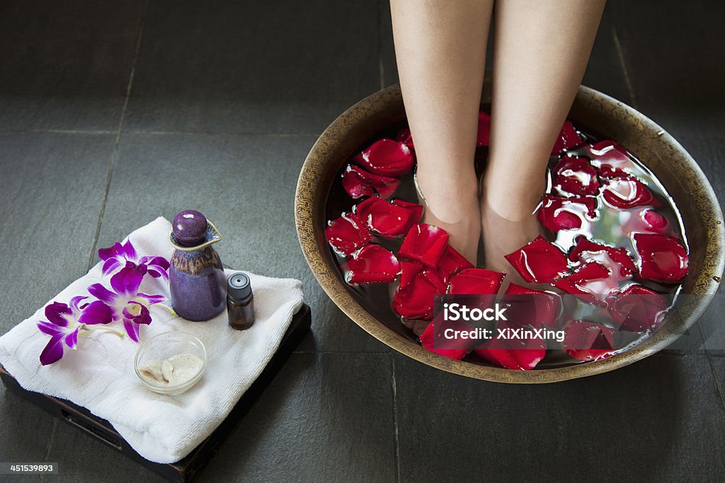 Woman soaking her feet in rose petal water Woman's Feet Soaking in Water with Rose Petals Bathtub Stock Photo