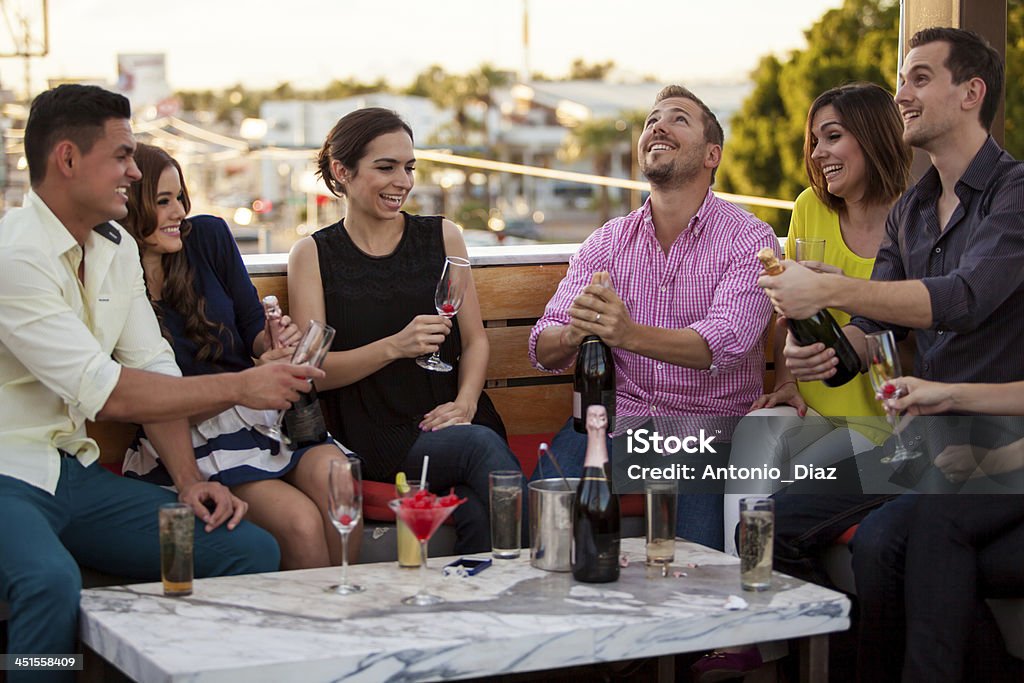 Popping up some champagne Group of Latin friends celebrating and popping a bottle of champagne at a terrace Champagne Cork Stock Photo