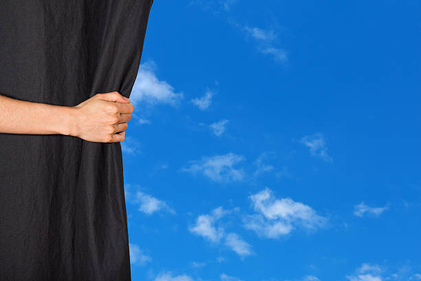istock Hand opening a curtain with blue sky behind it 451581327