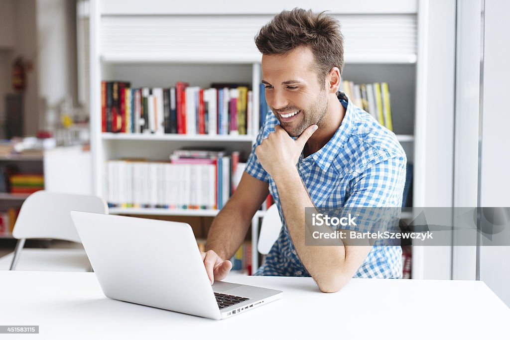 A man smiling while facing his laptop Casual man working on laptop in library University Student Stock Photo