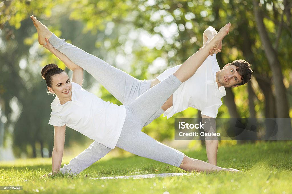 Couples Yoga, man and woman doing exercises in the park Couples Yoga, man and woman doing yoga exercises in the park Active Lifestyle Stock Photo