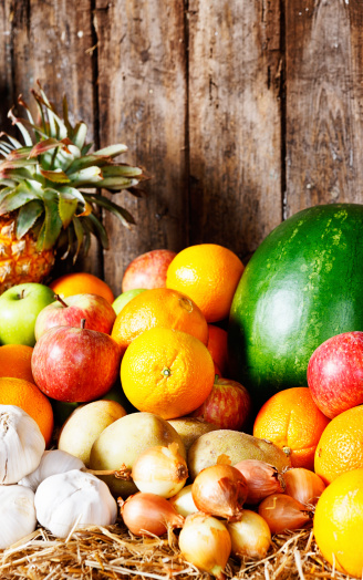 On a worn wooden background sits a selection of appetizing fresh winter fruits and vegetables. Copy space on the wood.