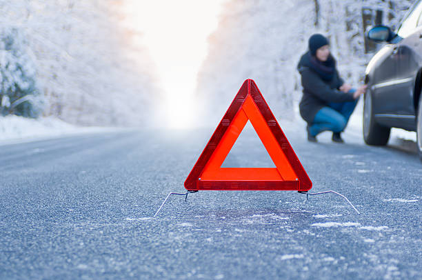 Winter driving - car breakdown Car breakdown on a country road in winter. Woman crouching beside her car, inspecting the front wheel. hazard sign photos stock pictures, royalty-free photos & images