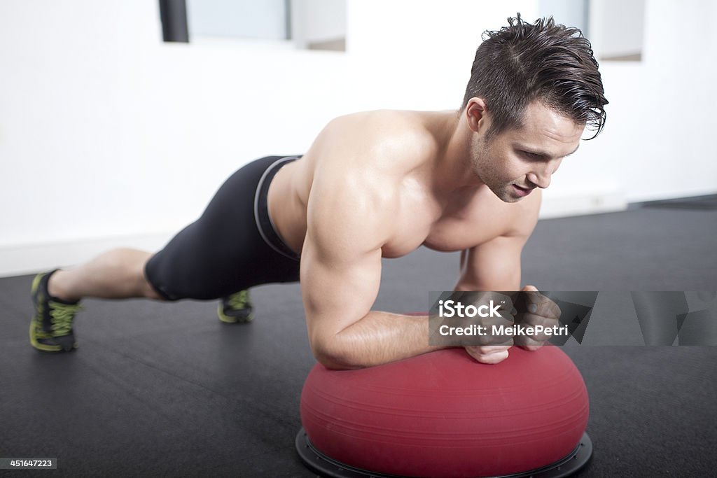 Plank on Bosu Gymnastic Ball Male athlete performing a plank on top of a gymnastic ball as core exercise. Abdominal Muscle Stock Photo