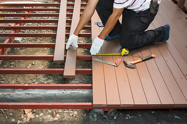 Worker installing wood floor for patio in construction site.