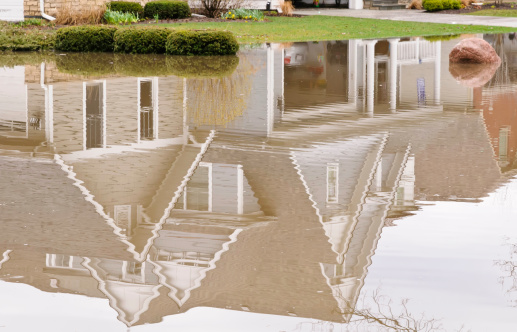 Part of suburban house reflected in flood waters over lower yard and street in the American Midwest