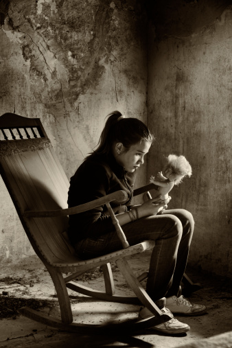 Lonely child playing with an old doll, sitting in a rocking chair