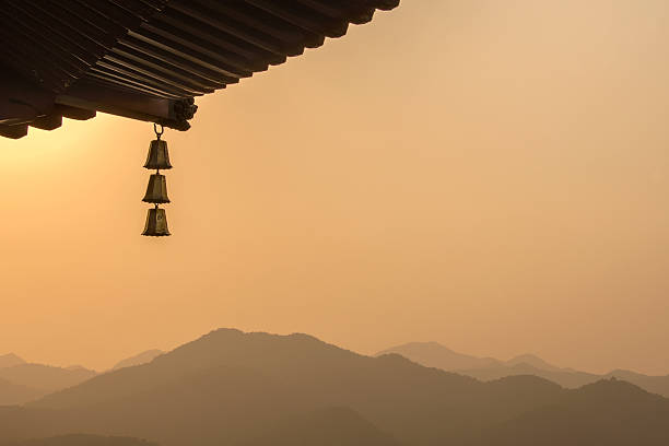 Close up of a Chinese pagoda with bells and a mountain range at sunset.