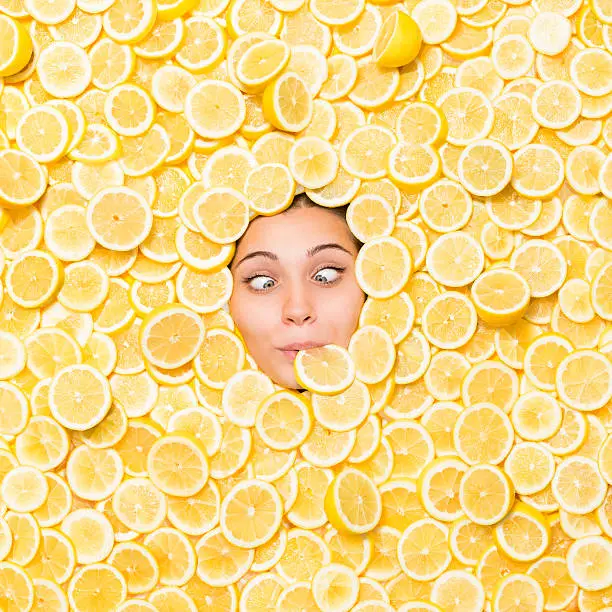 Portrait Of Cross-eyed Woman Lying In Lemons With Slice In Her Mouth