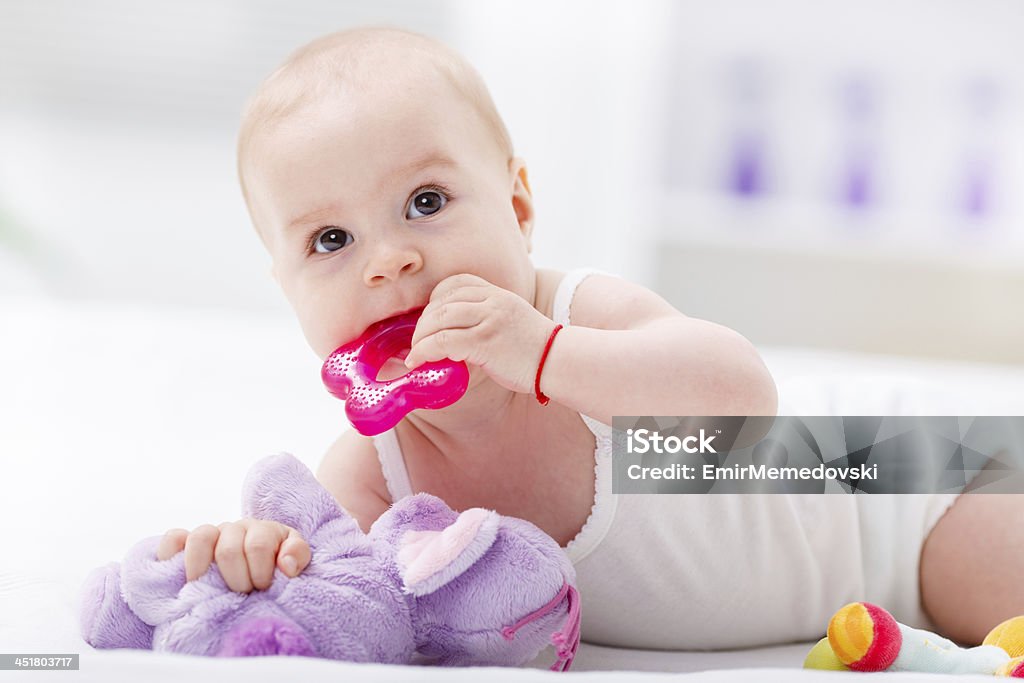 Bebé masticar un primer juguete en la cama. - Foto de stock de Bebé libre de derechos