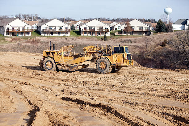 Residential or Commercial Development with Scraper A low aerial view of a residential or commercial development area with a scraper moving dirt. The foreground offers copy space with tire and caterpillar tracks, the background is a duplex neighborhood and water tower. road scraper stock pictures, royalty-free photos & images