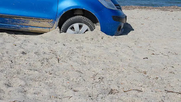 Car with front wheels stuck in the sand on beach.