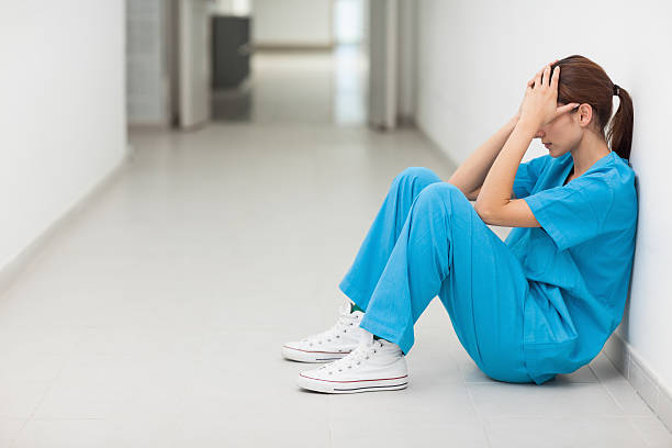 istock Nurse sitting in a corridor while holding her head 451860349