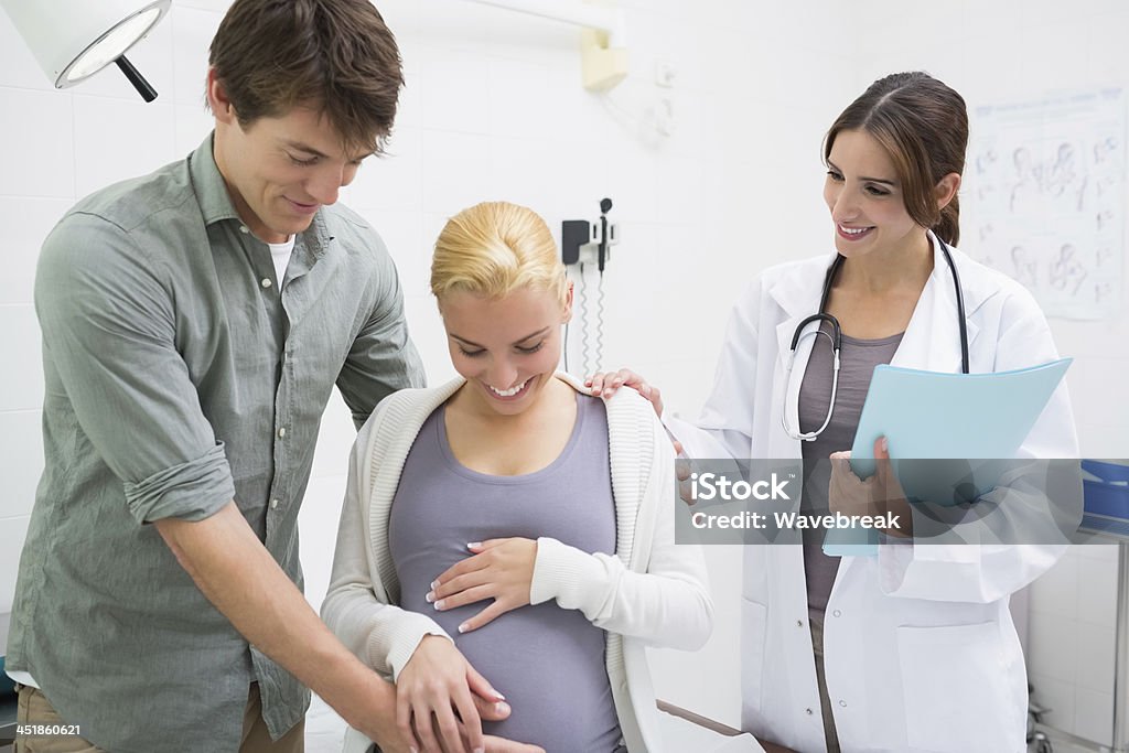 Doctor with a pregnant woman and her husband Doctor in an examination room with a pregnant woman her husband 20-29 Years Stock Photo