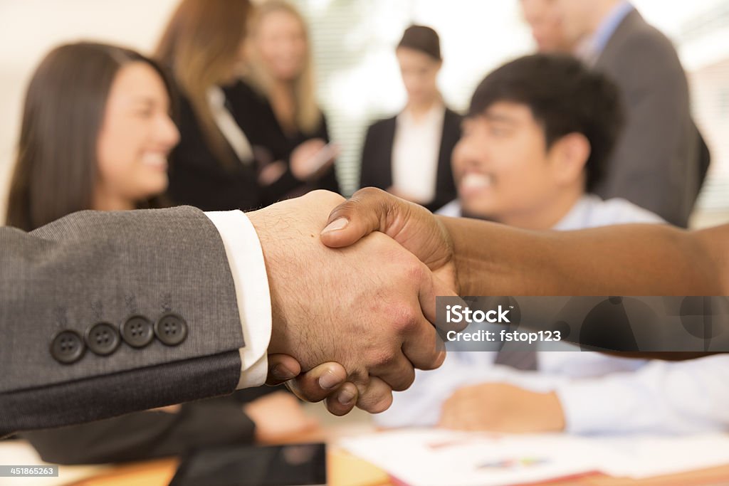 Business:  People shake hands during office meeting. Business people shake hands during business deal.  Coworkers meet behind them. Adult Stock Photo