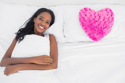 Woman lying in bed beside heart cushion in bedroom at home