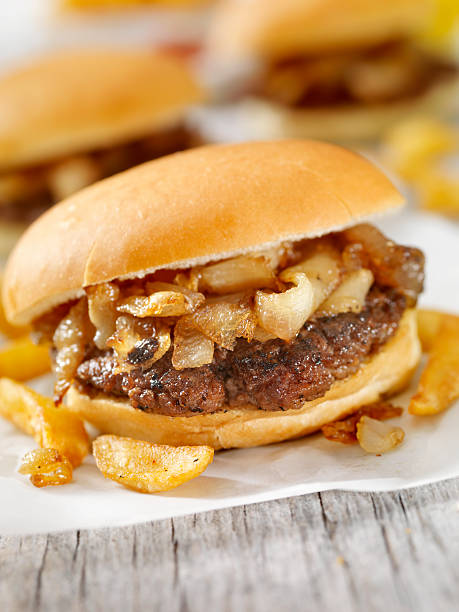 Close up shot of male hands with protective gloves putting caramelized onion above the bun as he preparing vegan burger ,on top of a takeout box