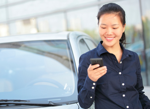 asian businesswoman use smart phone leaning on car outside of office building