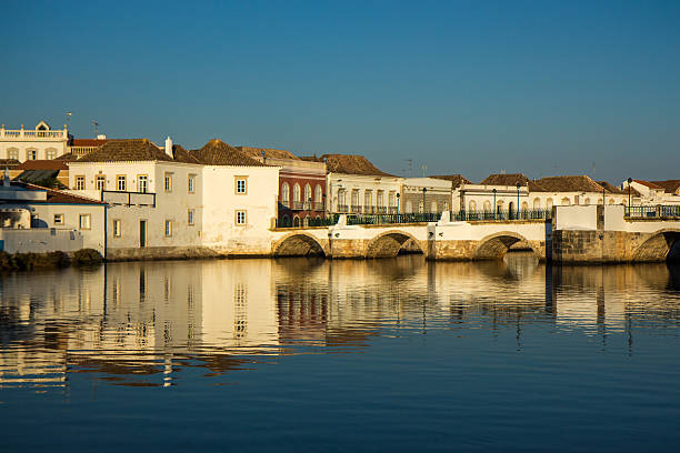 View overlooking river of Tavira old town and bridge in the Algarve, Portugal during golden hour of sunset reflected in the water.