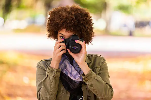 Autumn outdoor portrait of beautiful African American young woman holding a digital camera - Black people