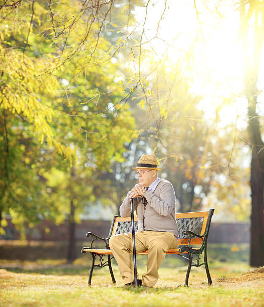 istock Sad senior man with cane on bench in a park 451937403