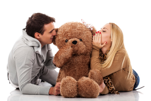 Young couple whispering teddybear isolated on white in studio