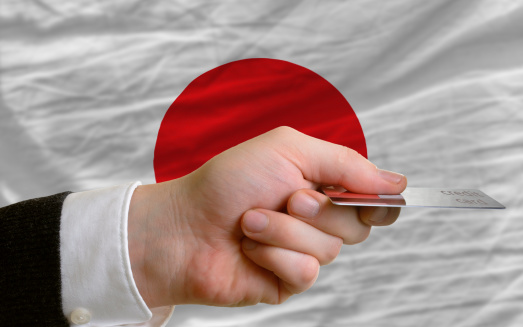 man stretching out credit card to buy goods in front of complete wavy national flag of japan